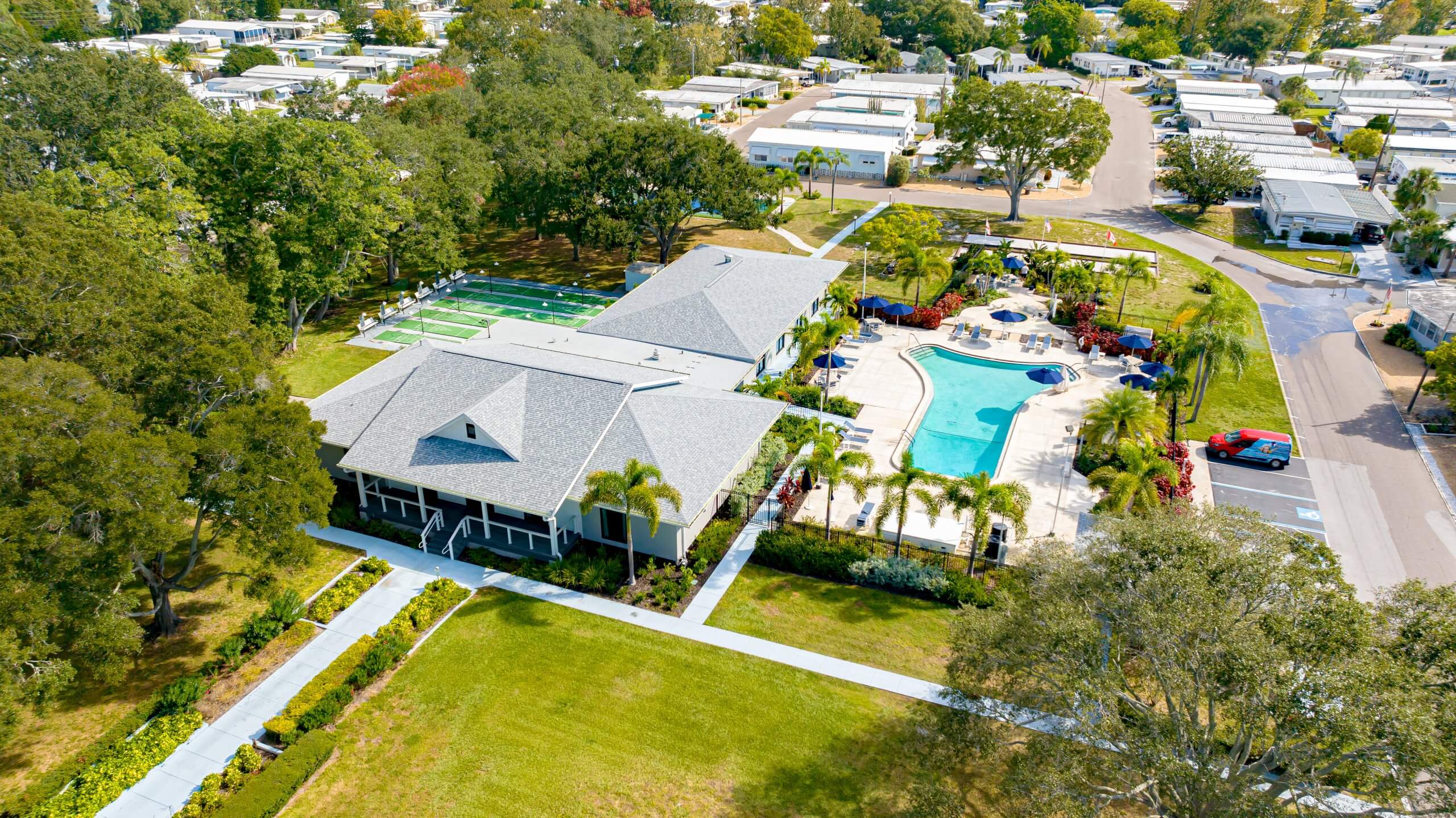 Aerial view of a community center with pool, shuffleboard courts, amidst residential mobile homes.