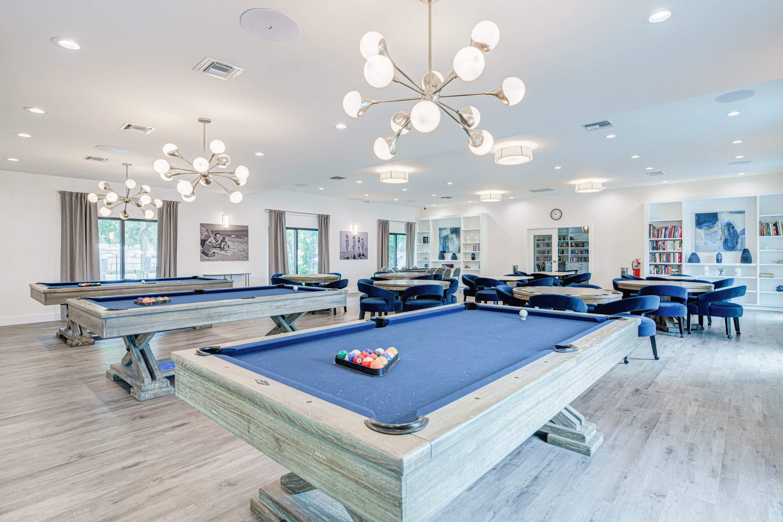 Recreational room with billiard tables, modern lighting, seating areas, and a bookshelf.