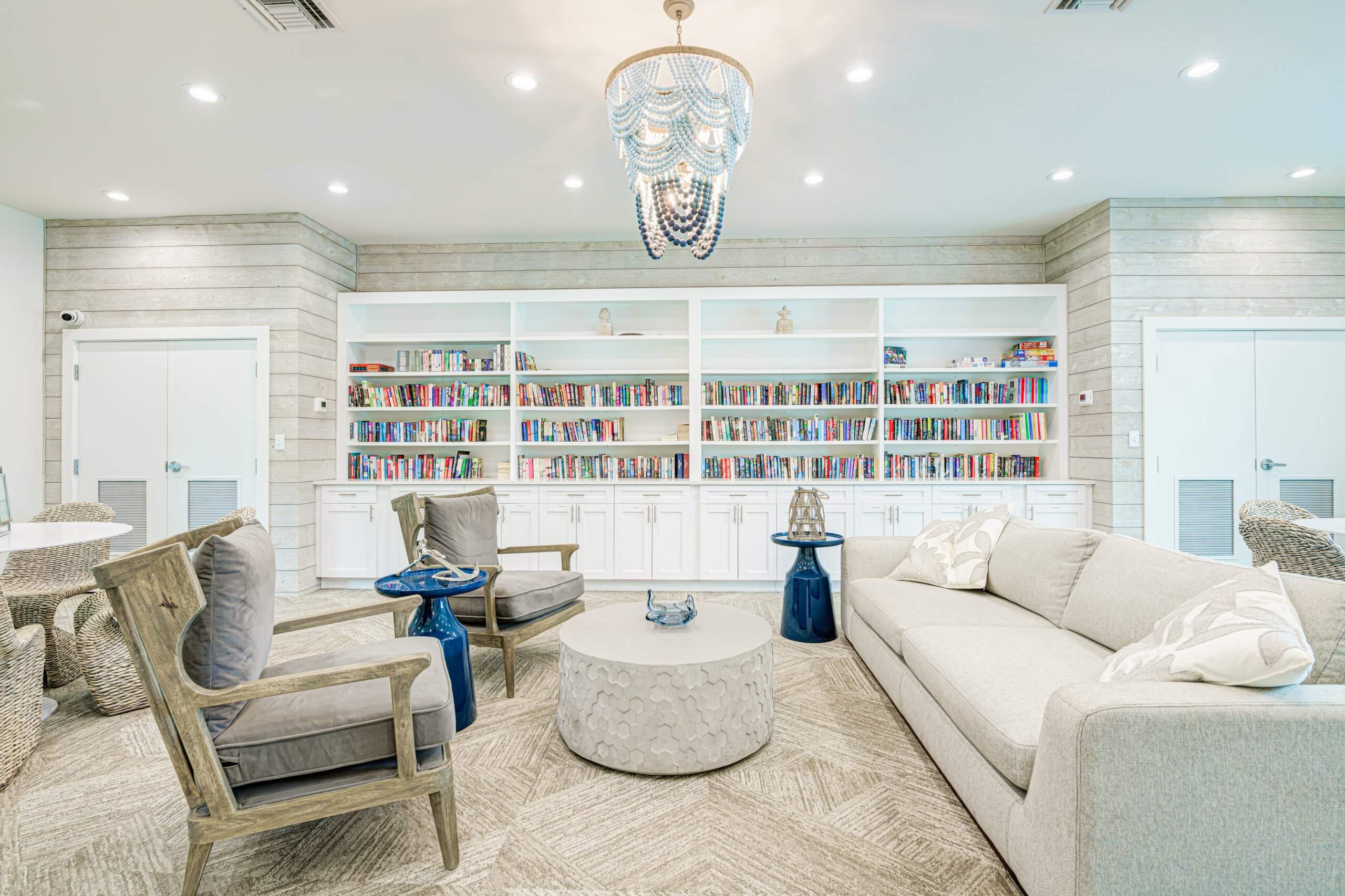 Cozy community library with plush seating, a large bookshelf, and a chic chandelier.